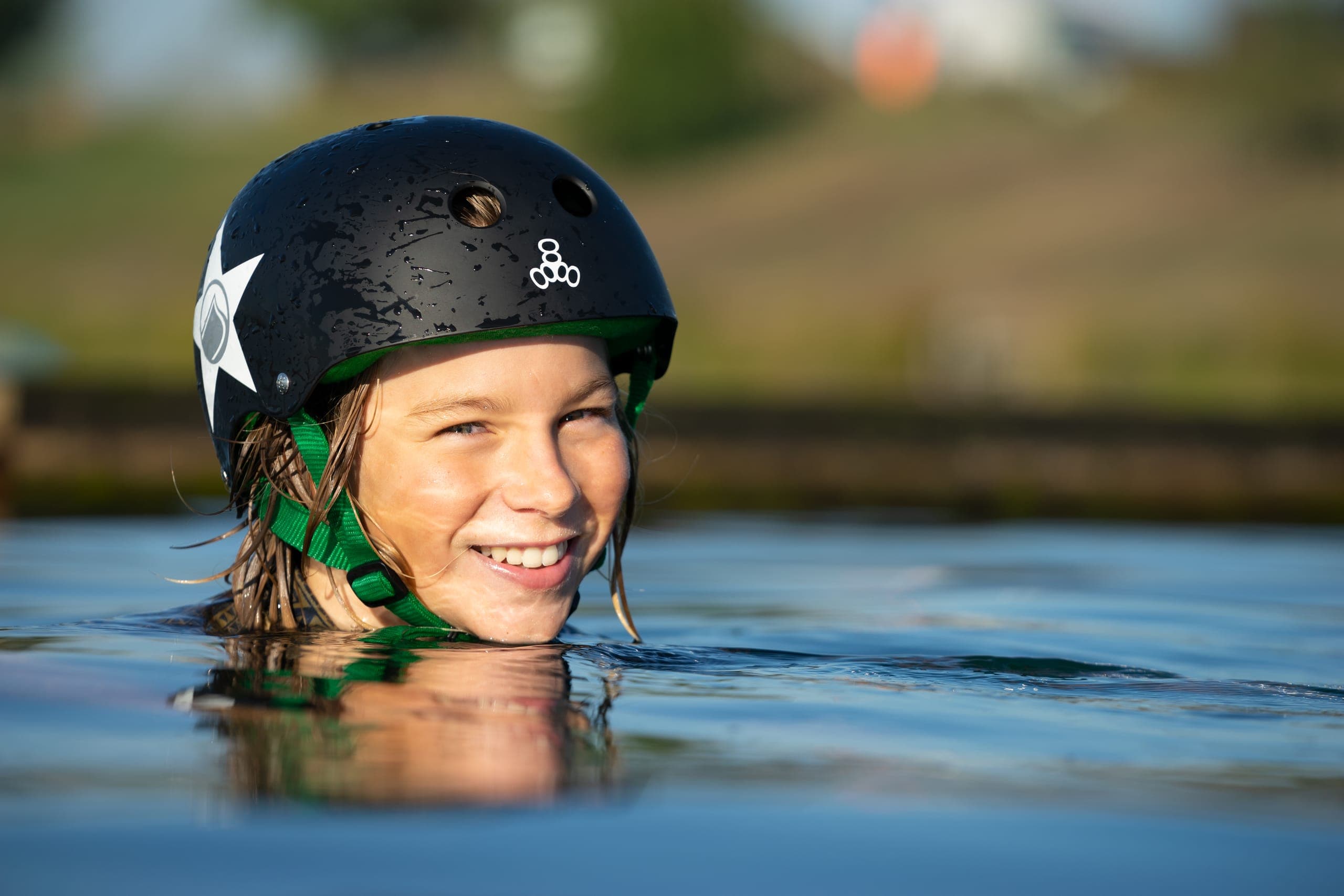 Mädchen mit Helm lacht im Wasser, nur Kopf und Helm schauen heraus